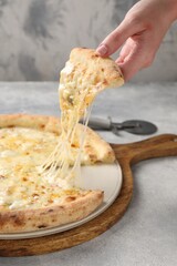 Woman taking piece of delicious cheese pizza at light grey table, closeup