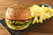 Burger with delicious patty and french fries on wooden table, closeup