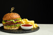 Burger with delicious patty, french fries and sauce on gray table against black background, space for text