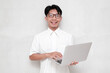 © herukru - Portrait man in glasses smiling happily holding laptop looking at camera, wearing white shirt isolated