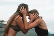 © moonmovie - Portrait of a mother and her teenage daughter standing on the beach near the ocean during sunset. A woman kisses her daughter on the forehead. Teen girl laugh. Mothers Day.