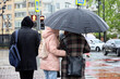 Two women with one umbrella standing on city street on red traffic light background. Rainy weather in spring