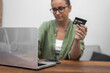 Credit card in hand, a woman with glasses takes care of online payments and shopping via her laptop. 