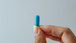 © john - Fingers holding a blue mini pill with text  , white soft background