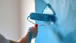 Closeup of a Hand Holding a Painter's Roller with Blue Paint Brushing a White Wall for Home