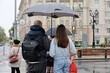 People with umbrellas standing on city street on red traffic light background. Rainy weather in spring