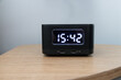 A black clock with the time 15:42 on it sits on a wooden table