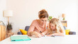 Happy young mother helping her daughter doing school homework at home - Education and childhood life style concept