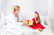 Blonde mother giving gift box to little cute surprised girl wearing red dress and crown on head, sitting on bed wishing daughter happy birthday, celebrating holiday.