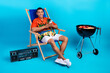 Full length photo of funky positive guy dressed print shirt relaxing lounge chair grilling meat chatting device isolated blue color background