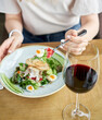 A woman sits at a table with food and a glass of Burgundy wine