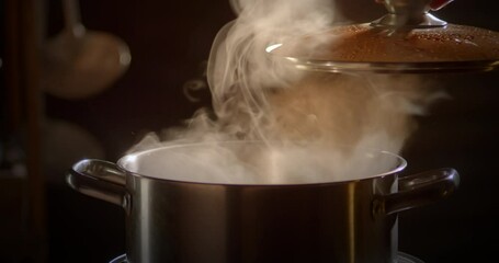 Wall Mural - Slow motion scene of a boiling pot steams up as a chef opens the lid of a cooking pot in a restaurant.