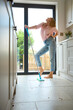 Woman At Home In Kitchen Striking Pose With Mop As She Does Housework