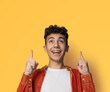 Excited black curly haired man in braces, open mouth, wear orange denim shirt advertise pointing show area for sales slogan text, isolated against yellow wall background. Dental care, ad concept.
