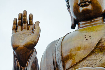 The image is a statue of Buddha, made of bronze, with his right hand raised in the Abhaya mudra, a gesture of fearlessness and protection