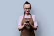 Portrait of 30s woman in apron holding smartphone in hands on grey background