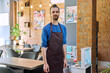 Young man worker, owner in apron looking at camera in restaurant, coffee shop