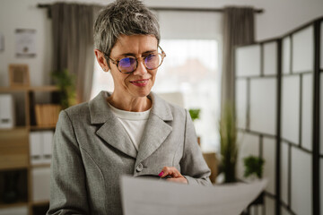 Portrait of mature woman stand and hold cup and document at office