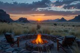 Fototapeta  - Majestic sunset behind rugged mountains with a glowing campfire in the foreground