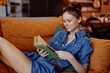 Woman in denim dress reading book on couch in coffee shop interior