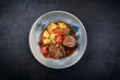 Traditional slow cooked German wagyu beef roulades with vegetable and gnocchi served in spicy red wine sauce as top view in a Nordic design plate with copy space