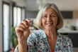 Cheerful senior woman proudly displays a set of house keys with a blurred modern home interior background, showcasing a moment of new homeownership or independent living