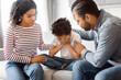 African American man and woman are seated on a couch, accompanied by a child. Parents comforting their upset crying child, home interior