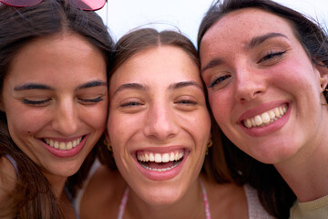 Wall Mural - Close-up faces portrait of group pretty gen z Caucasian women looking smiling at camera. Three European beautiful female friends posing happy for selfie photo. Summer vacations cheerful travel people