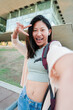 © Jose Calsina - Vertical. Happy asian female teenage student laughing and shooting a selfie with a cellphone. Young chinese woman smiling and taking a portrait with a smart phone. korean girl gesturing the peace sign