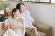 家のリビングでソファーに座って外を眺める若いアジア人夫婦
