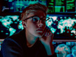 A young adult with short blonde hair and round glasses poses thoughtfully in a data center, surrounded by screens displaying global data. 