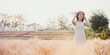 © Satori Studio - Woman in a white dress and straw hat standing amidst a golden wheat field at sunset.