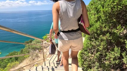 Wall Mural - A woman and a man are walking up a set of stairs, with the woman carrying a bag. The scene is set against a backdrop of a blue ocean, creating a serene and peaceful atmosphere.