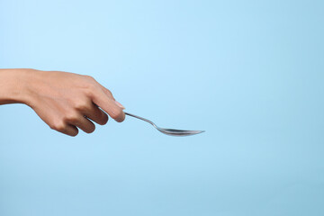 Woman's hand holds a stainless spoon on a blue pastel background.