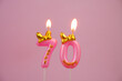 Burning pink birthday candle with gold bow and letters happy on pink background. Number 70.	