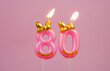 Burning pink birthday candle with gold bow and letters happy on pink background. Number 80.	