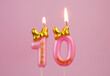 Burning pink birthday candle with gold bow and letters happy on pink background. Number 10.	