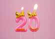Burning pink birthday candle with gold bow and letters happy on pink background. Number 20.	