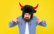 Brutal man wearing bull hat isolated on yellow. Bearded angry man in party hat. Bearded and brutal hipster. Caucasian aggressive guy in bull hat. Aggressive and angry man with beard. Point finger