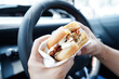 Asian woman driver hold and eat hamburger in car, dangerous and risk an accident.