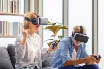 Cheerful senior caucasian couple playing video game using virtual reality glasses and joystick