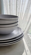 Stack of white plates and bowls by a window with sheer curtains