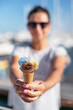 HHappy, smiling woman holding ice cream cone with colorful ice cream balls. Sunny sea coastline at the background.
