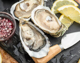 Fototapeta  - Opened raw oysters with sauce and lemon slices on gray stone serving board. Delicacy food.