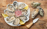 Fototapeta  - Opened raw oysters with sauce and lemon slices on plate on wooden table. Top view.