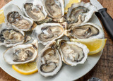 Fototapeta  - Opened raw oysters with sauce and lemon slices on plate on wooden table. Top view.