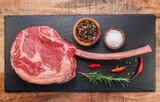 Fototapeta  - Raw rib steak with bone or tomahawk steak with seasonings on slate serving plate. Flat lay.