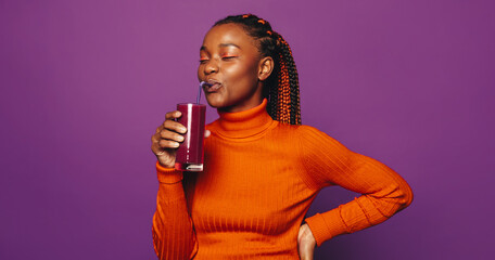 Wall Mural - Cheerful woman holding a colorful smoothie, standing on a vibrant purple background