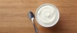 A top down view of a cup and spoon containing fresh and thick sour cream on a table with a blank space nearby for text in the image. Copy space image. Place for adding text and design