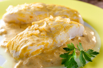 Two hake fillets with curry sauce on green dish